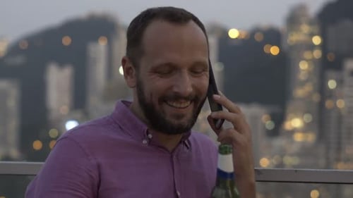 Man on Phone Drinks Beer with City Lights