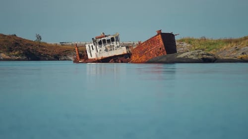 Ein rostiges, verlassenes Schiffswrack, das in der Nähe der felsigen Küste versunken ist, mit dem ruhigen Wasser und der Küste in der