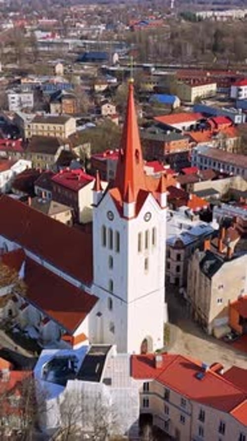 Vertical aerial view of a white church tower rising above Cesis old town, with red rooftops, narrow