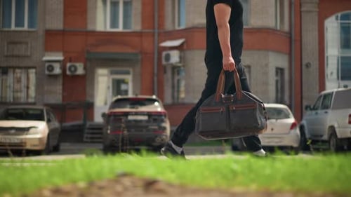Man Carries a Bag Walking Past City Buildings