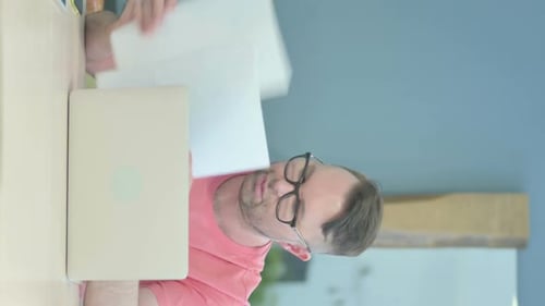 Man Works At Laptop Computer and Reads Documents