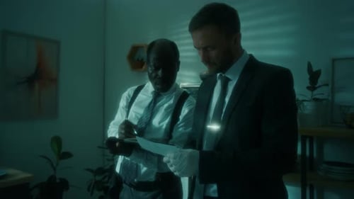 Men Examine Paperwork in Moody, Dim Office