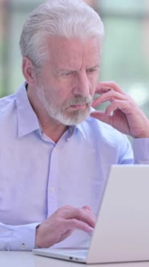 Senior Man Uses Laptop, Concentrating at Work