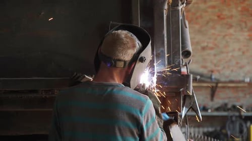 Worker Welding Metal Parts Together in Garage