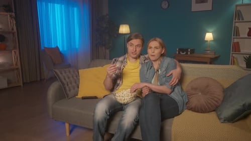 A Couple Sits Hugging on the Couch with a Plate of Popcorn and Watching a Movie The Man Comments on