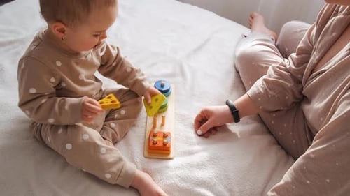 Nahaufnahme eines kleinen Kindes beim Spielen von Lernspielen für kleine Kinder mit Mutter auf dem Bett im