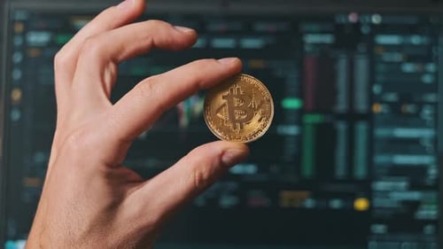 Bitcoin in Trader-Hand auf dem Hintergrund des Kryptowährungs-Börsendiagramms auf dem Laptop