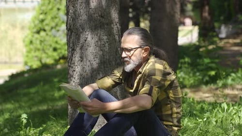 Homme cultivé et intellectuel lisant un livre dans le parc.
