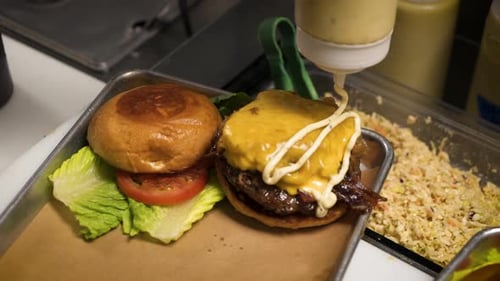 Chef drizzles special sauce on top of cheeseburger, Cook finishes dressing burger, slow motion 4K
