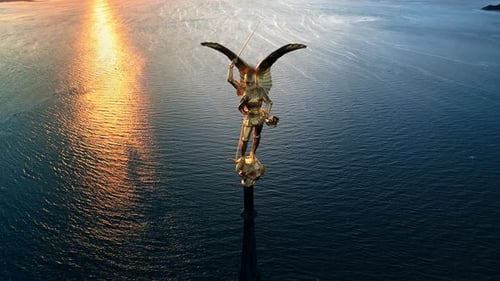 Aerial drone view of statue of Archangel Michael atop the spire of Mont-Saint-Michel at sunset in No