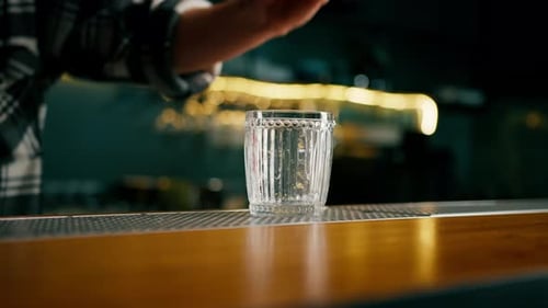 A glass with an ice cube stands impressively on the bar The initial stage of making a cocktail