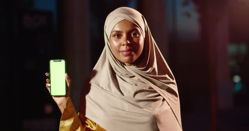 Portrait of Young Arab Smiled Beautiful Woman in Hijab Standing at Street and Showing Smartphone