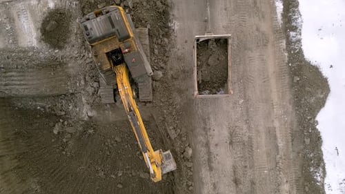 A aerial view of a excavator loading dirt into the back of a dump truck pup