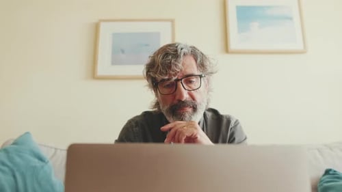 Close up, elderly man working on laptop sitting on the sofa in the living room