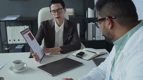 Female Clinical Manager Discussing Report with Doctor at Office Meeting