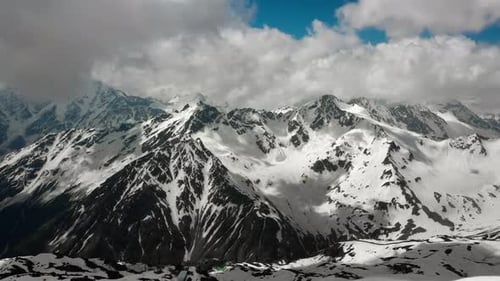 Air flight through mountain clouds over beautiful snow-capped peaks of mountains and glaciers.