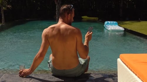 Man Relaxing by Tropical Pool Using Phone