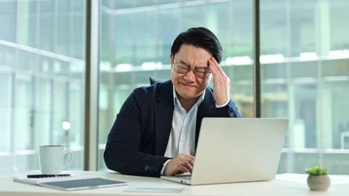 Stressed Businessman Suffering From Headache While Working on Laptop in Office