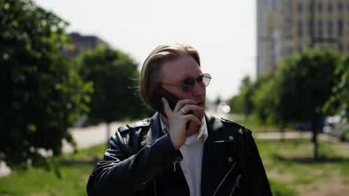 A Stylish Man in a Black Leather Jacket Walks Through the Park Near an Apartment Complex Summer Mood