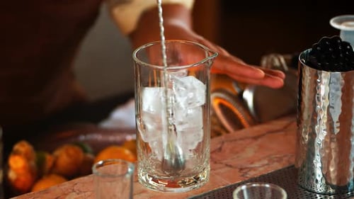 Bartender Stirs Ice Cubes in Cocktail Glass at Bar