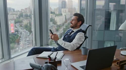 Happy bearded businessman in modern office reading good news on smartphone