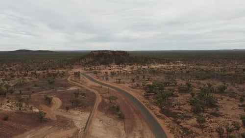 Drone ascending over a remote bushland revealing a Hill and lookout in Australia. Sealed road leads