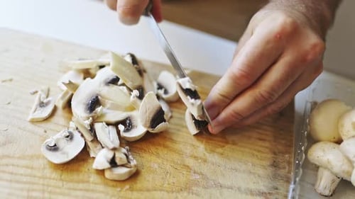 Hands Slicing White Mushrooms on a Wooden Board