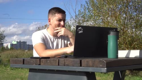 A Man Works on a Laptop While Sitting on a Bench Outdoors Work Remotely