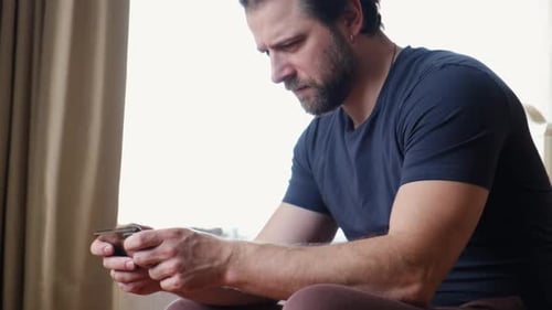 Man Seated Using Cellphone Indoors by Window