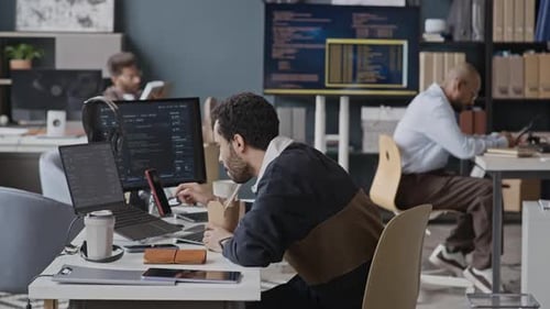 Middle Eastern Developer Eating Takeout Lunch at Desk and Coding on Laptop