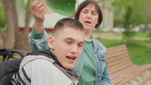 Woman Adjusts Cap on Teenager in Wheelchair in Park