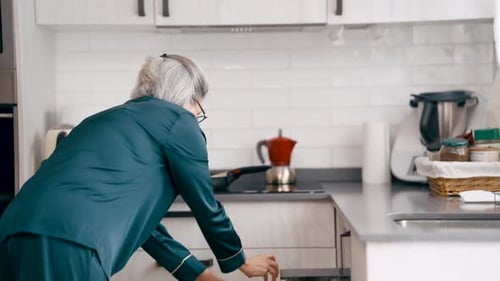 Elderly Woman Loading the Dishwasher in the Morning Kitchen