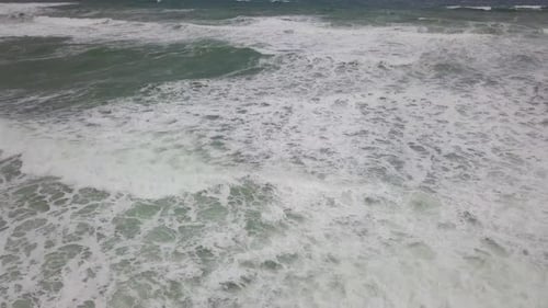 Stormy sea with waves breaking, white foam and beach sand dragged into the sea