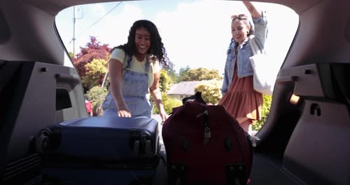 Two Young Women Loading Luggage into Car Trunk