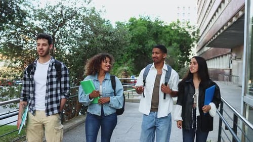 Diverse university students chat while walking on campus with books and backpacks