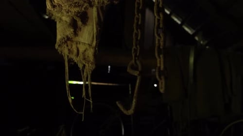 Rusty chains hang from the ceiling and dangle in an abandoned basement with shadow, a metal chain