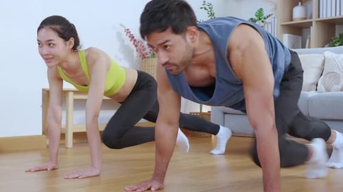 Happy young asian couple workout with doing mountain climbers exercise together in living room.