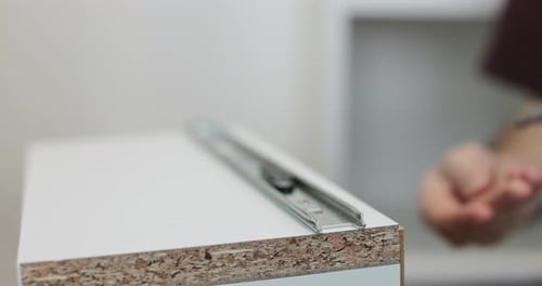 Homme utilisant une perceuse électrique pour fixer une glissière de tiroir en métal à un meuble pendant l'assemblage