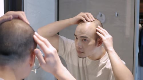 Man Inspects Hair in Bathroom Mirror at Home
