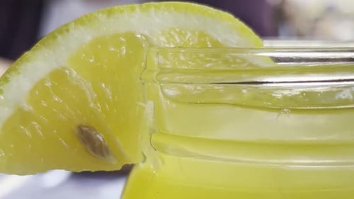 Close-up of a slice of yellow lemon on the rim of a glass jar filled with lemonade.