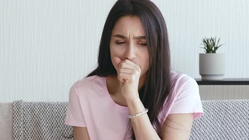 Young Woman Coughing while Sitting on a Couch