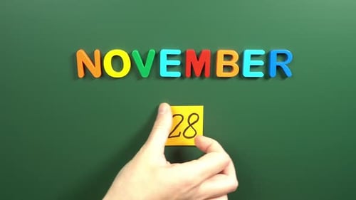 Hand sticking a sticker 28 November calendar day on school board. 28 date of November. Twenty