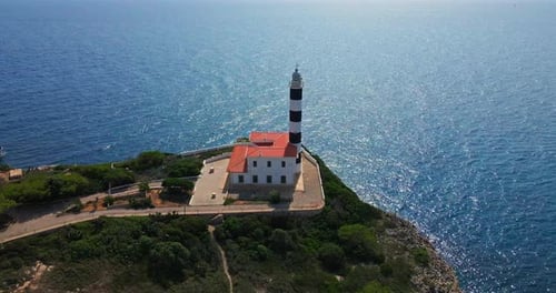 Aerial orbit of Spanish lighthouse with sparking ocean and reveal of village during summer on hot tr