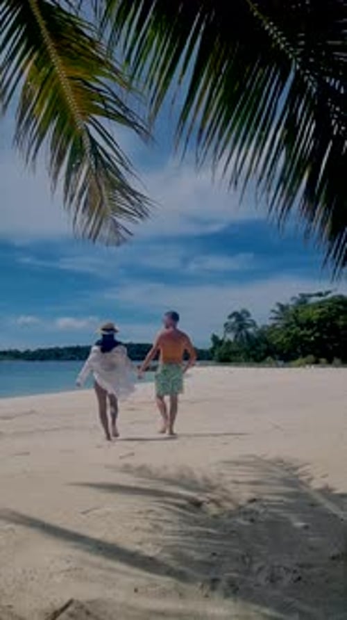 a Mature Couple Walking on a Tropical White Sandy Beach with Palm Trees in Thailand