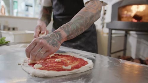 Chef Adding Cheese to Pizza Base with Tomato Sauce