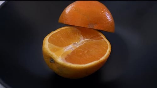 Sartén a cámara lenta alrededor cortada por la mitad (naranja) en un plato negro