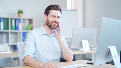 Young handsome bearded caucasian man employee with severe toothache. male worker indoors suffers