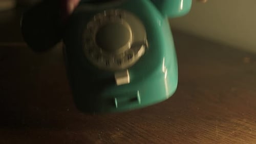 A hand in a coat puts an old analog corded telephone on the secretary.