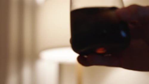 Hand Holding a Glass of Dark Beverage with Ice