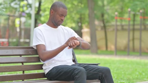Man Interacting with Smartwatch on Park Bench